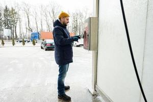 uomo addebiti il dispositivo scatola con i soldi a un' se stesso servizio lavare nel freddo tempo atmosferico. foto