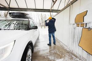 uomo lavaggio alto pressione acqua americano suv auto con tetto cremagliera a se stesso servizio lavare nel freddo tempo atmosferico. foto