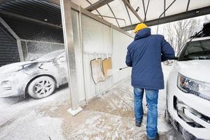 uomo lavaggio alto pressione acqua americano suv auto con tetto cremagliera a se stesso servizio lavare nel freddo tempo atmosferico. foto