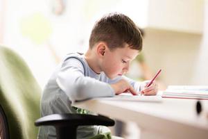 ragazzo ragazzo studiando a casa e fare scuola compiti a casa, distanza apprendimento formazione scolastica , seduta a tavolo. foto