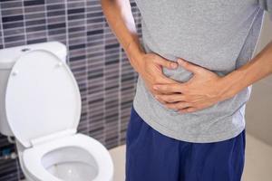 uomini avere mal di stomaco e uso loro mani per hold loro stomaco nel il bagno. stipsi o colon cancro foto