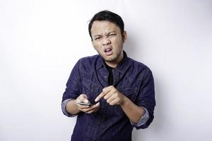 il arrabbiato e pazzo viso di asiatico uomo nel blu camicia Tenere il suo Telefono isolato bianca sfondo. foto