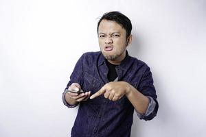 il arrabbiato e pazzo viso di asiatico uomo nel blu camicia Tenere il suo Telefono isolato bianca sfondo. foto