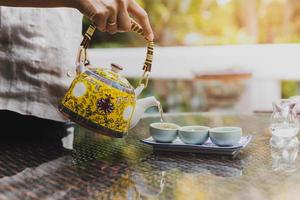 donna mano scrosciante erbaceo tè in un' pentola su naturalmente sfocato sfondo. foto