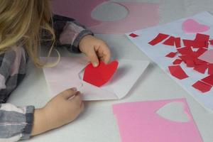 bambino Tenere lettera con rosso carta cuore amore lettera per San Valentino giorno, regalo per madri giorno, piccolo ragazza mettere fatto a mano cuore dentro busta, vacanza saluti a partire dal figlia, finta su per amore auguri foto