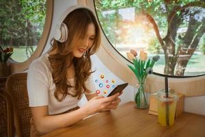 bellissimo donna indossare cuffie utilizzando inteligente Telefono con sociale media nel il bar. sociale media e digitale in linea. sorridente di femmina con stile di vita, tecnologia su vacanza concetto. messa a fuoco su mano. foto