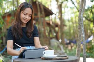 asiatico donne siamo contento per sedersi e opera nel un' caffè negozio. Là siamo verde alberi circondato di natura. attività commerciale pianificazione è un' bene idea. foto