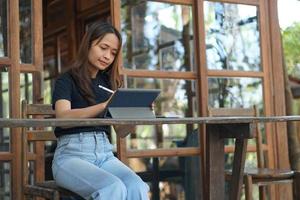 asiatico donne siamo contento per sedersi e opera nel un' caffè negozio. Là siamo verde alberi circondato di natura. attività commerciale pianificazione è un' bene idea. foto