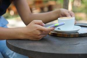 asiatico donna guardare a guadagni su sua Telefono a un' caffè negozio dove lei può partire per opera. in mezzo verde natura foto