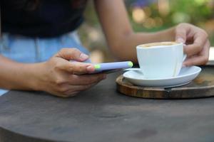 asiatico donna guardare a guadagni su sua Telefono a un' caffè negozio dove lei può partire per opera. in mezzo verde natura foto