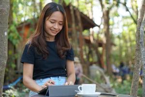 asiatico donne siamo contento per sedersi e opera nel un' caffè negozio. Là siamo verde alberi circondato di natura. attività commerciale pianificazione è un' bene idea. foto