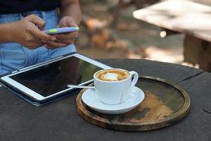 asiatico donna guardare a guadagni su sua Telefono a un' caffè negozio dove lei può partire per opera. in mezzo verde natura foto