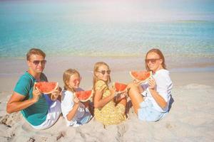 contento famiglia mangiare anguria su il spiaggia. foto