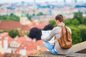 giovane uomo con un' città carta geografica e zaino sfondo europeo città. caucasico turista guardare a il carta geografica di europeo città con bellissimo Visualizza di attrazioni. foto