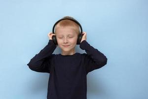 biondo ragazzo ascolta per musica nel cuffie con chiuso occhi su un' blu sfondo foto