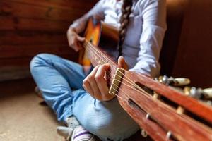 giovane fricchettone donna mani giocando chitarra a casa. adolescente ragazza apprendimento per giocare canzone e scrittura musica nel sua camera. passatempo, stile di vita, relax, strumento, tempo libero, formazione scolastica concetto. foto