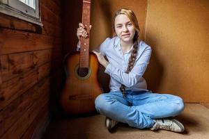 giovane fricchettone donna seduta su pavimento e giocando chitarra a casa. adolescente ragazza apprendimento per giocare canzone e scrittura musica nel sua camera. passatempo, stile di vita, relax, strumento, tempo libero, formazione scolastica concetto. foto