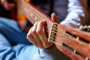 giovane fricchettone donna mani giocando chitarra a casa. adolescente ragazza apprendimento per giocare canzone e scrittura musica nel sua camera. passatempo, stile di vita, relax, strumento, tempo libero, formazione scolastica concetto. foto