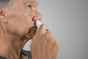 anziano uomo utilizzando un' nasale spray per il suo asciutto naso foto