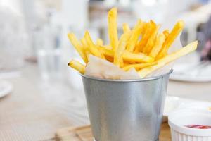 patatine fritte, avvolte con carta in un piccolo secchio inossidabile su un tavolo di legno, messa a fuoco selettiva foto