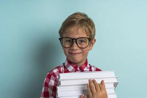 un' ragazzo con occhiali, con libri nel il suo mani su un' turchese sfondo. indietro per scuola. foto