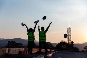 silhouette Immagine di ingegnere civile e costruzione lavoratore gettare su sicurezza casco e costruzione disegno contro il sfondo di surreale costruzione luogo nel crepuscolo o buio paesaggio urbano. foto