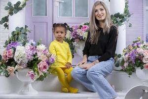 multietnico mamma e figlia siamo seduta su il veranda di il Casa. allegro madre con poco figlia di africano nazionalità. famiglia a partire dal diverso gare. foto