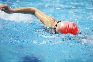 il atleta nuotate nel il piscina nel un' rosso nuoto cap. un' uomo nuotate nel blu acqua. foto