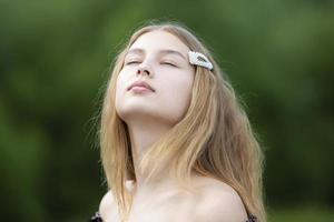 un' bellissimo ragazza con lungo capelli chiuso sua occhi su un' estate sfondo. il viso di un' biondo adolescenziale ragazza. foto