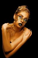 moda arte d'oro pelle. ragazza modello con festivo d'oro fascino brillante professionale trucco. creativo trucco con d'oro Foglio. foto