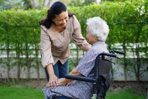 il caregiver aiuta il paziente con disabilità della donna anziana asiatica seduto su una sedia a rotelle nel parco, concetto medico. foto