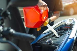 uomo riempimenti il carburante in il gas serbatoio di motociclo a partire dal un' rosso scatola metallica o plastica carburante può .Manutenzione riparazione moto concetto ,selettivo messa a fuoco. foto