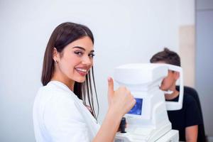 femmina oculista utilizzando macchina per controllo occhio vista nel clinica. poco ragazzo guardare a attrezzatura e medico analisi occhio allievo nel ottico negozio. concetto di occhio cura e Salute. foto