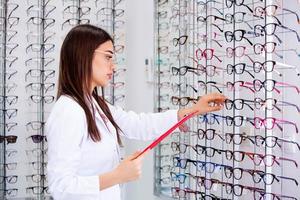 attraente femmina oculista scrittura dati per un' appunti, Lavorando nel un ottico negozio. assistenza sanitaria e medicina concetto foto