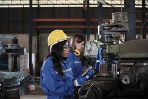 un industriale lavoratori squadra nel protettivo e sicurezza uniformi e elmetti, maschio gestore, e femmina colleghi opera con metallo macchine nel produzione fabbrica. professionale produzione ingegnere. foto