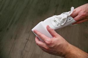 un' uomo pulisce bianca scarpe da ginnastica con melamina spugna. foto