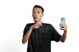 asiatico uomo indossare nero formazione maglietta, con un' contento eccitato gesto mentre guardare a il smartphone schermo. isolato di bianca sfondo foto