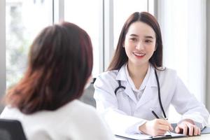 asiatico professionale medico femmina chi indossa medico cappotto parla con donna paziente per sua paziente anziano nel visita medica camera, assistenza sanitaria concetto nel ufficio di Ospedale. foto