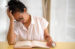 giovane asiatico donna seduta solo nel loro camera, viso giù pianto, mentre avere il vuoto libro mettere su il scrivania. solitudine, sensazione fatica e ansia concetto. foto