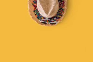 bianca occhiali da sole e cannuccia cappello colorato a strisce su luminosa giallo sfondo. estate concetto foto