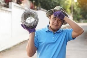 asiatico uomo lavoratore detiene rotolo di spinato filo, si sente stanco. concetto, costruzione attrezzo. spinato filo è Usato per rendere recinzioni , sicuro proprietà ,Fare confine per mostrare il territorio di la zona. foto