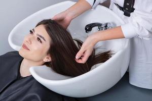 professionale parrucchiere lavaggio capelli di giovane donna nel bellezza salone. vicino su di donna di capelli nel bellezza salone, acconciatura concetto foto