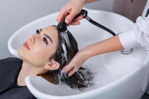 professionale parrucchiere lavaggio capelli di giovane donna nel bellezza salone. vicino su di donna di capelli nel bellezza salone, acconciatura concetto foto