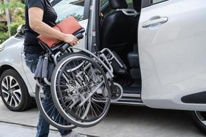 donna asiatica che piega e solleva la sedia a rotelle nella sua auto. concetto di accessibilità. foto