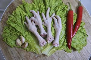 crudo pollo piedi su un' chopping tavola con lattuga, rosso peperoncini, e aglio. fresco e biologico pollo piedi. superiore Visualizza foto