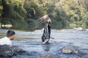 asiatico ragazzi siamo la spesa loro tempi liberi di immersione, nuoto, lancio rocce e attraente pesce nel il fiume insieme felicemente. passatempo e felicità di bambini concetto. foto