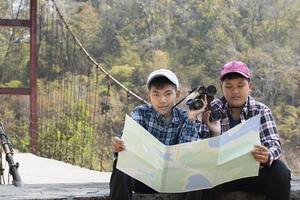 asiatico giovane adolescente ragazzi hold nazionale parco carta geografica, lettura dettagli di osservazione uccelli prima utilizzando loro binocolo per orologio il uccello quale seduta su brunch e volante nel il cielo, estate vacanza concetto. foto