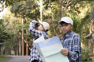 asiatico giovane adolescente ragazzi hold nazionale parco carta geografica, lettura dettagli di osservazione uccelli prima utilizzando loro binocolo per orologio il uccello quale seduta su brunch e volante nel il cielo, estate vacanza concetto. foto