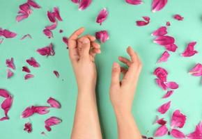 Due mani di un' giovane ragazza con liscio pelle e rosso peonia petali foto