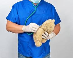 medico nel blu uniforme e bianca latice guanti Tenere un' Marrone orsacchiotto orso foto